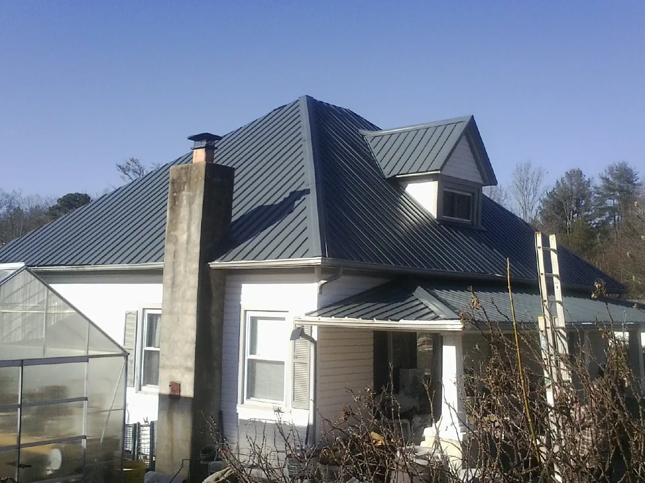 Dark blue standing seam metal roof on a white farmhouse with dormer — Slate & Tile Roof Repair by Roofing Brothers in Stephenson