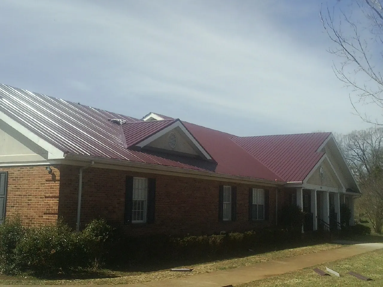 Red metal roof with gabled entries on a long brick building, from a Hail Damage Roof Repair job in Stephenson