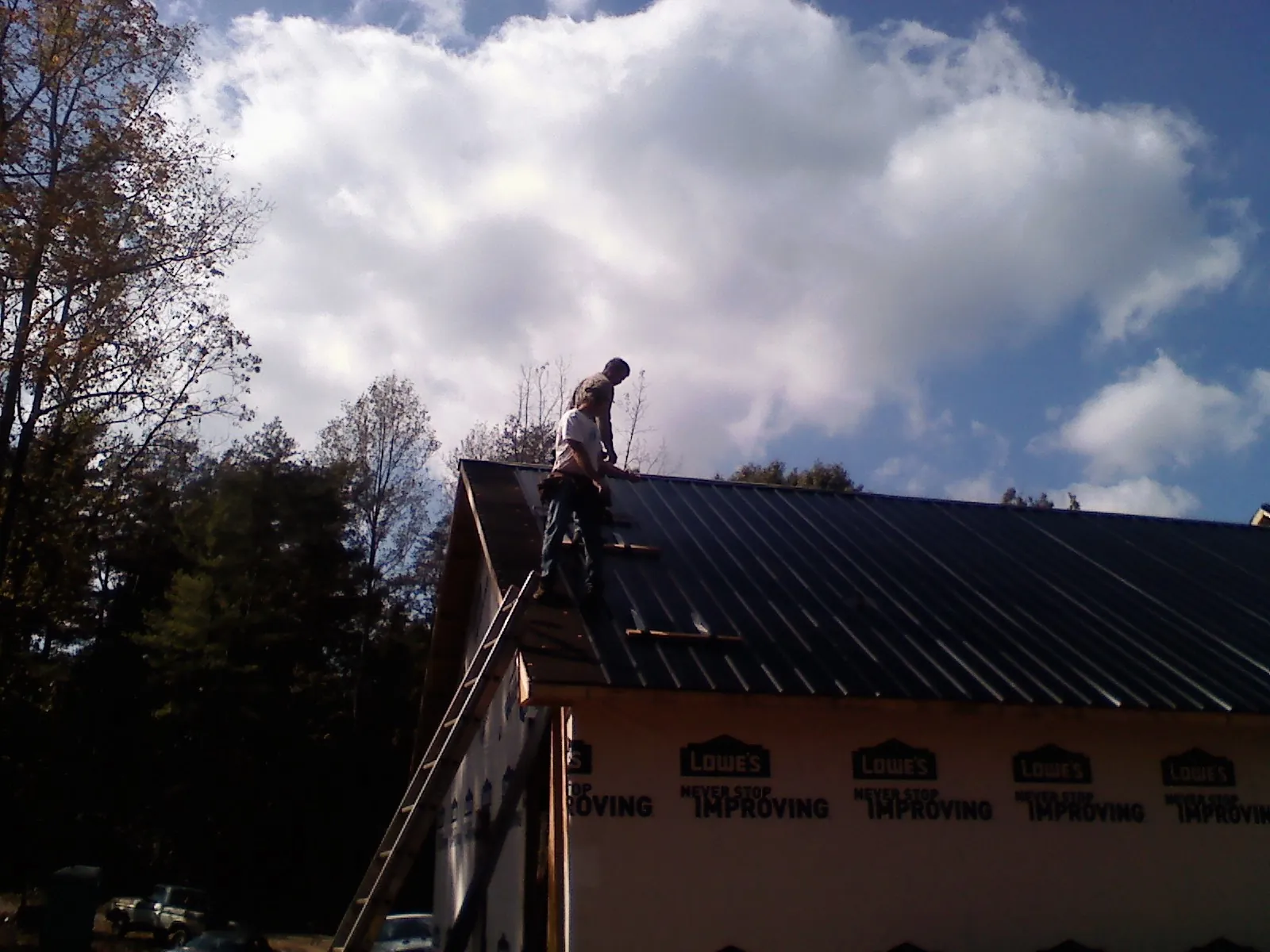 Roofer fastening dark metal panels high against a cloudy sky, from a Roof Inspection job in Stephenson