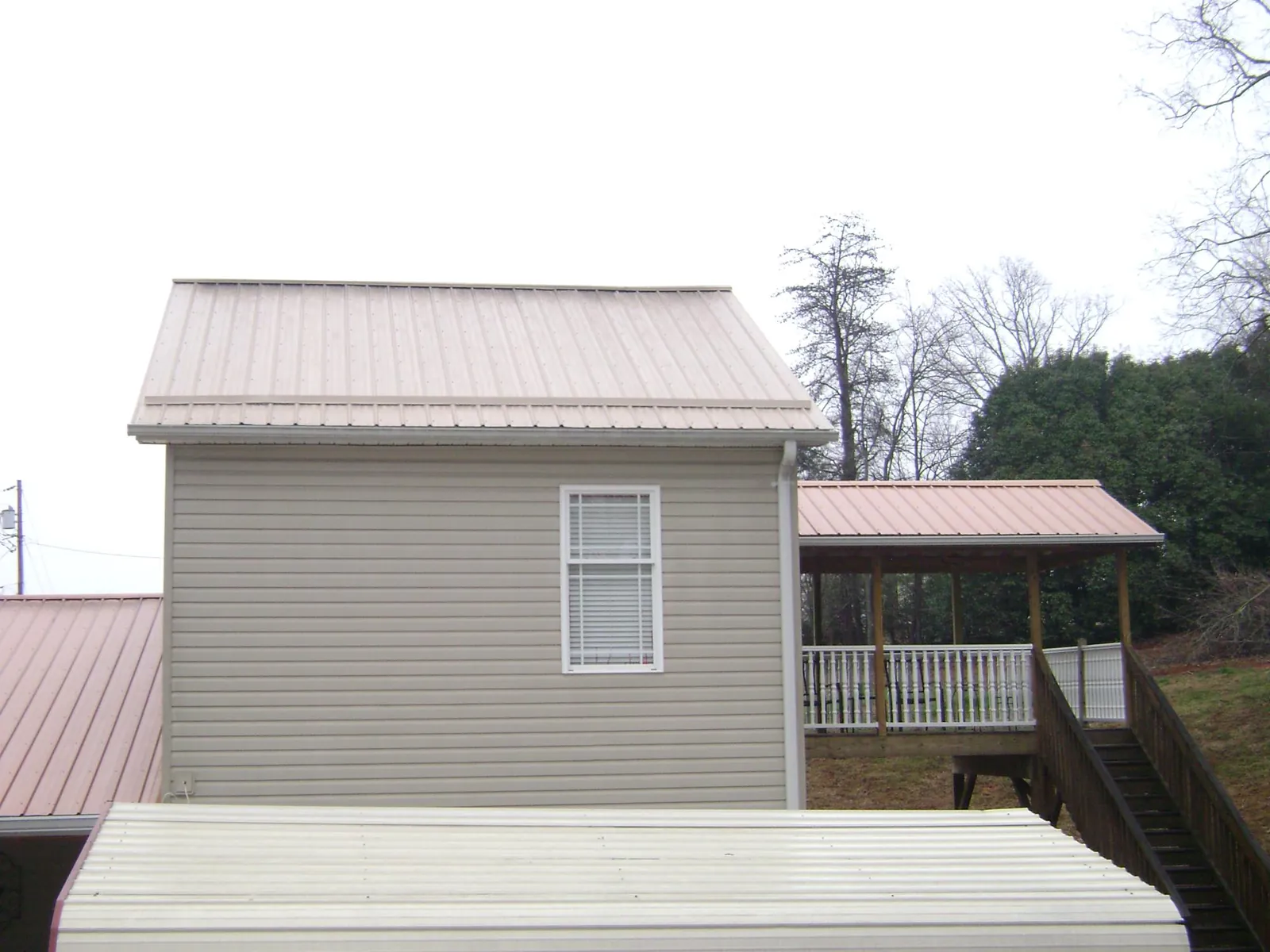 Tan metal roofs on a two story addition and attached porch, from a Roof Replacement job in Stephenson